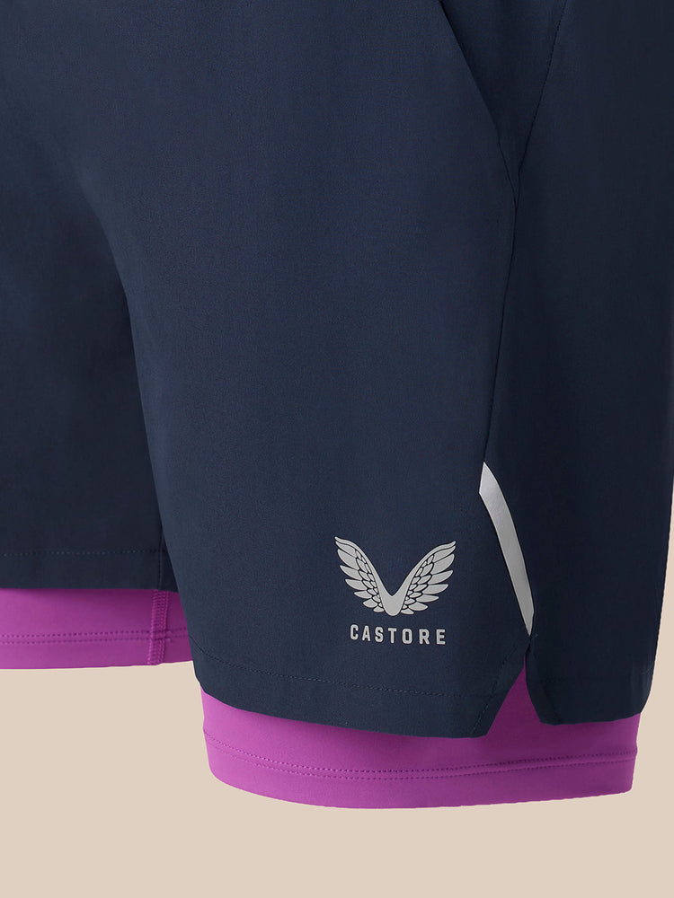 Close-up of dark navy athletic shorts with a purple inner layer peeking out at the hem, featuring a white Castore wing logo on the lower left leg.