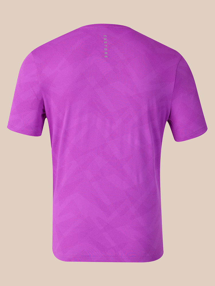 A purple short-sleeve athletic t-shirt shown from the back, featuring a subtle geometric pattern and a vertical 'CASTORE' logo printed in the center of the upper back, set against a solid beige background.