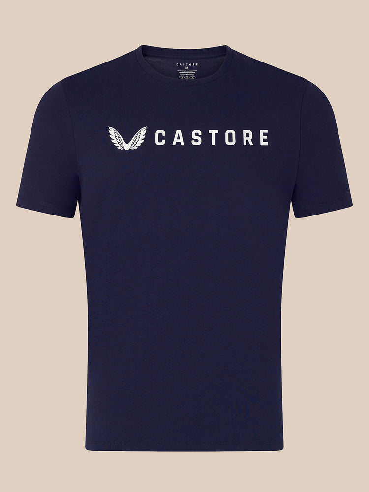 A navy blue short-sleeve crewneck t-shirt with a white Castore wing logo and brand name printed across the chest, displayed against a solid beige background.