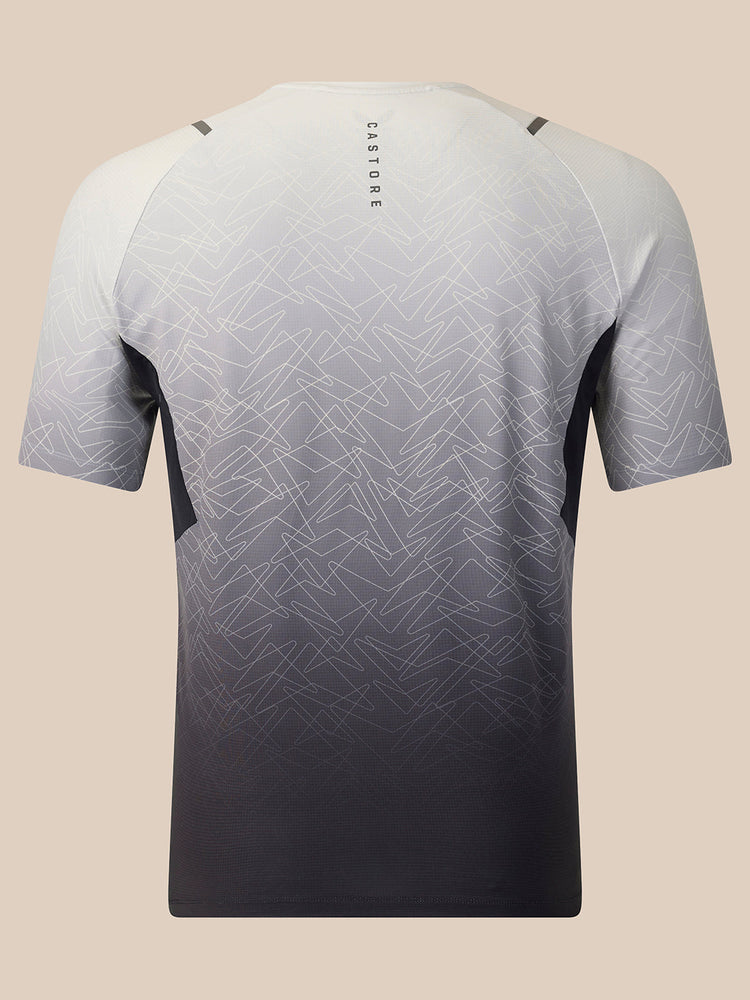 A short-sleeve athletic t-shirt shown from the back, featuring a gradient design that fades from white and light gray at the top to a dark charcoal gray at the bottom. The shirt has a subtle geometric pattern overlay and the brand name 'CASTORE' printed vertically on the upper back, set against a solid beige background.